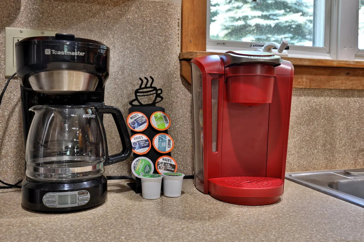 Close-up of a countertop coffee station featuring a coffee maker, red kettle, and coffee pods. The setup is both inviting and practical, ready for morning rituals or a comforting après-ski brew.