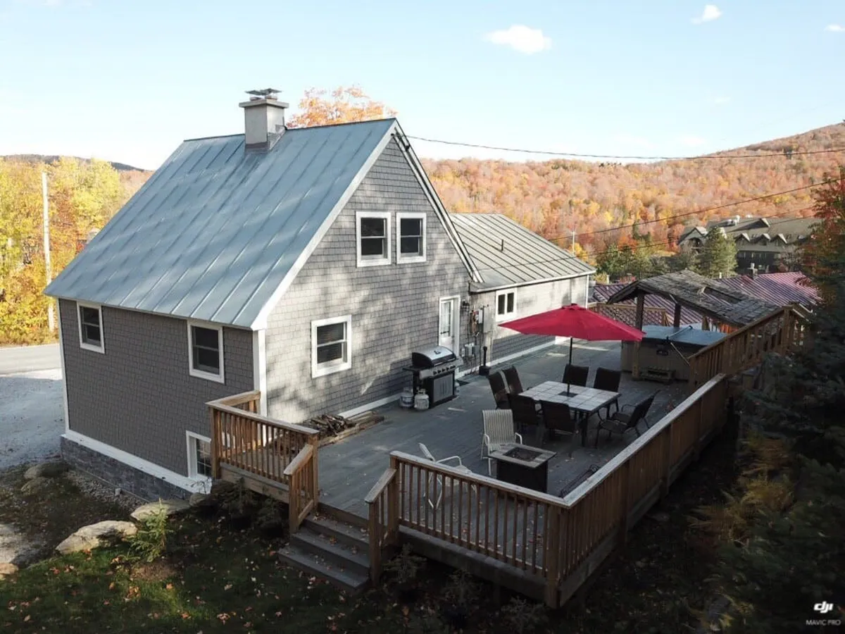This photo shows a wooden deck with patio furniture, a barbecue grill, a distinctive red umbrella, and lush autumn foliage surrounding the area. The scene captures the essence of friendly gatherings, outdoor dining, and enjoying nature at any time of day.