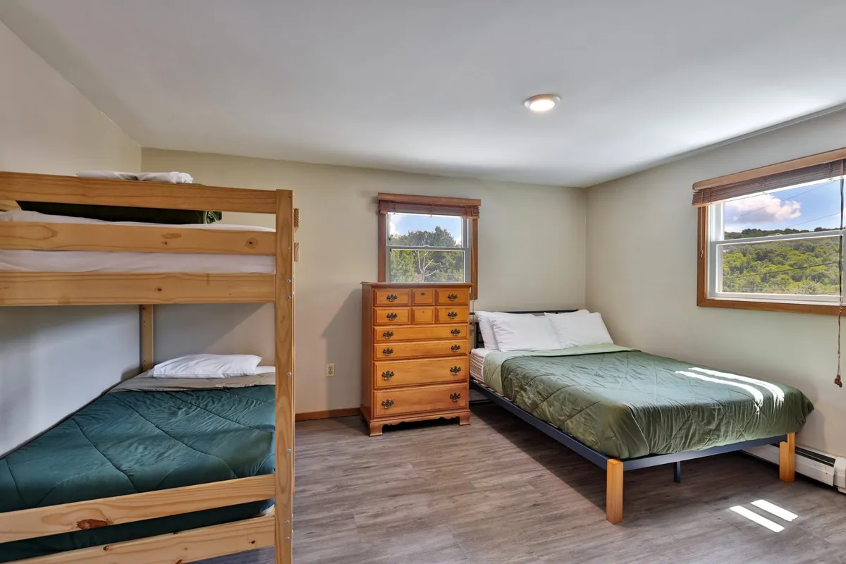 A comfortable family bedroom with a combination of a double bed, a bunk bed, a wooden dresser, and large windows with views outside. The room radiates a cozy and inclusive atmosphere, perfect for families or groups.