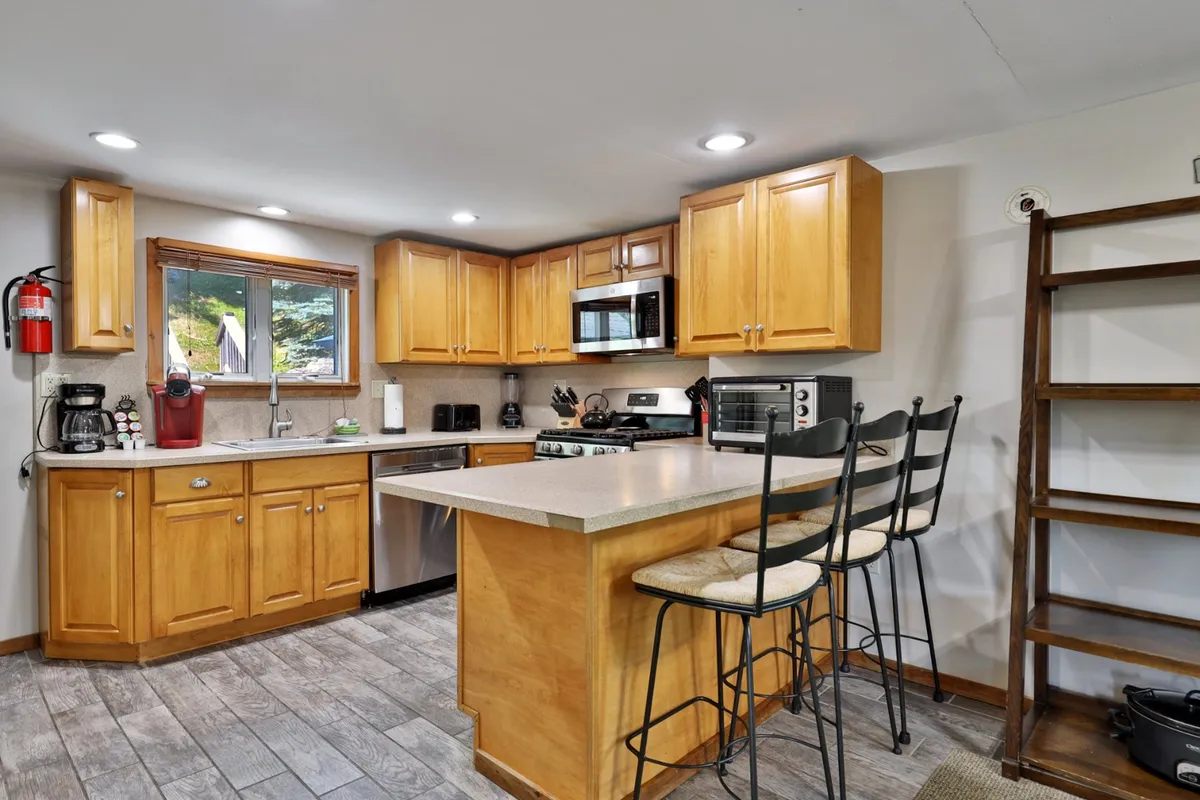 This image features a welcoming kitchen space with a central island, cabinets, and modern appliances. Bar stools line the island, inviting guests to gather while meals are prepared, and the overall layout encourages both cooking and social interaction.