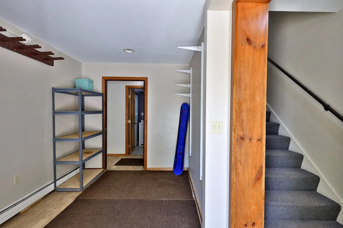 A practical area near the entrance, featuring shelves, a staircase, and a blue object likely used for storing gear. The space is organized and easily accessible, suggesting a spot where guests can drop off or collect outdoor equipment after activities.