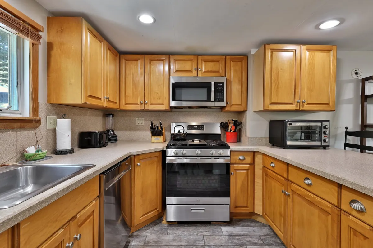 The photo showcases a kitchen with a stainless steel stove, wooden cabinets, a prominent sink, and ample countertop space, evoking a homey, functional cooking environment. The modern appliances stand ready for group feasts and culinary adventures.
