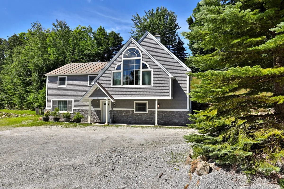 A modern chalet exterior with large windows, stone accents, and lush surrounding greenery. The spacious private yard is visible, offering ample space for outdoor relaxation and play. The atmosphere is serene and inviting, suggesting a welcoming spot for both guests and their pets.
