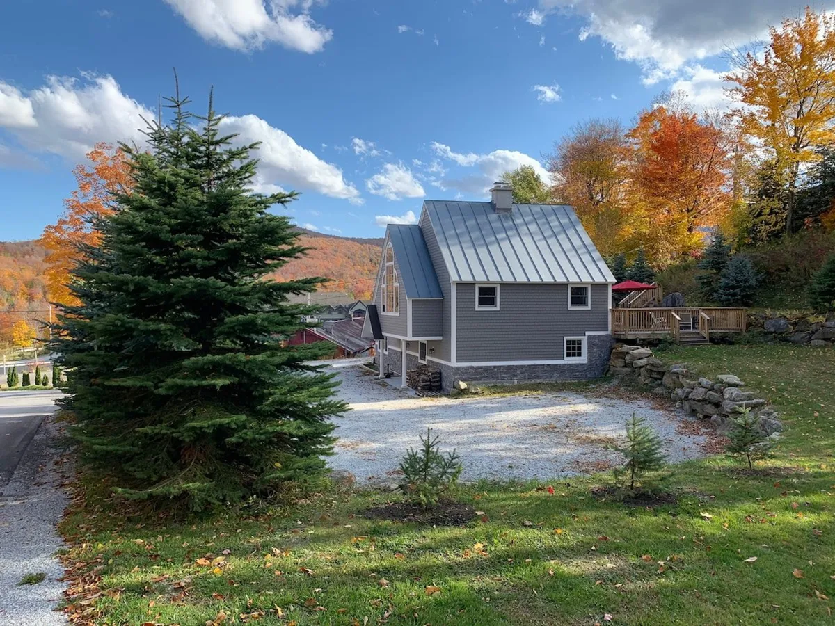 This exterior shot showcases the chalet with surrounding trees and mountain views, as well as the spacious deck, set against a peaceful backdrop. The setting hints at the property's proximity to ski slopes and its inviting outdoor gathering spaces.