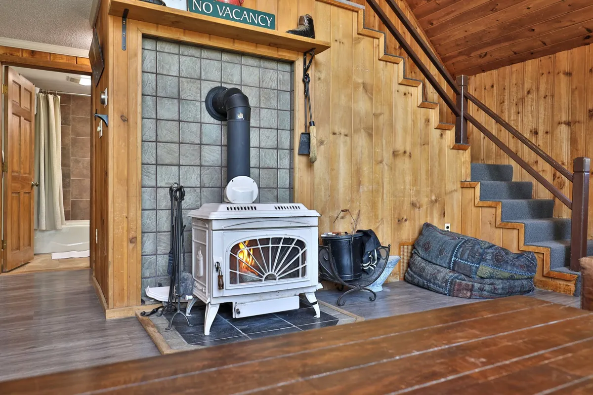A warm, inviting space with a wood stove, wood paneling, a staircase, and a seating area. The setting evokes relaxation after a day outdoors, with the wood stove promising warmth during cooler evenings.