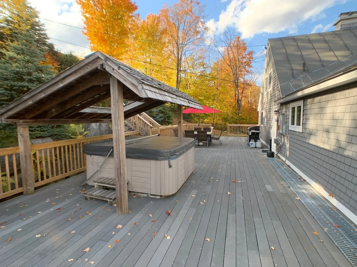 This image highlights the outdoor hot tub with people enjoying a relaxing soak, set against a backdrop of vibrant fall foliage. The outdoor dining area is also visible, creating a scene of social gatherings and relaxation. The overall atmosphere is relaxed and cheerful, emphasizing the appeal of après-ski soaks and evenings spent under the stars.
